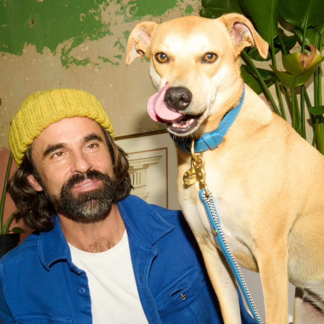 Man wearing a yellow beanie and blue jacket with a dog on a leash indoors.
