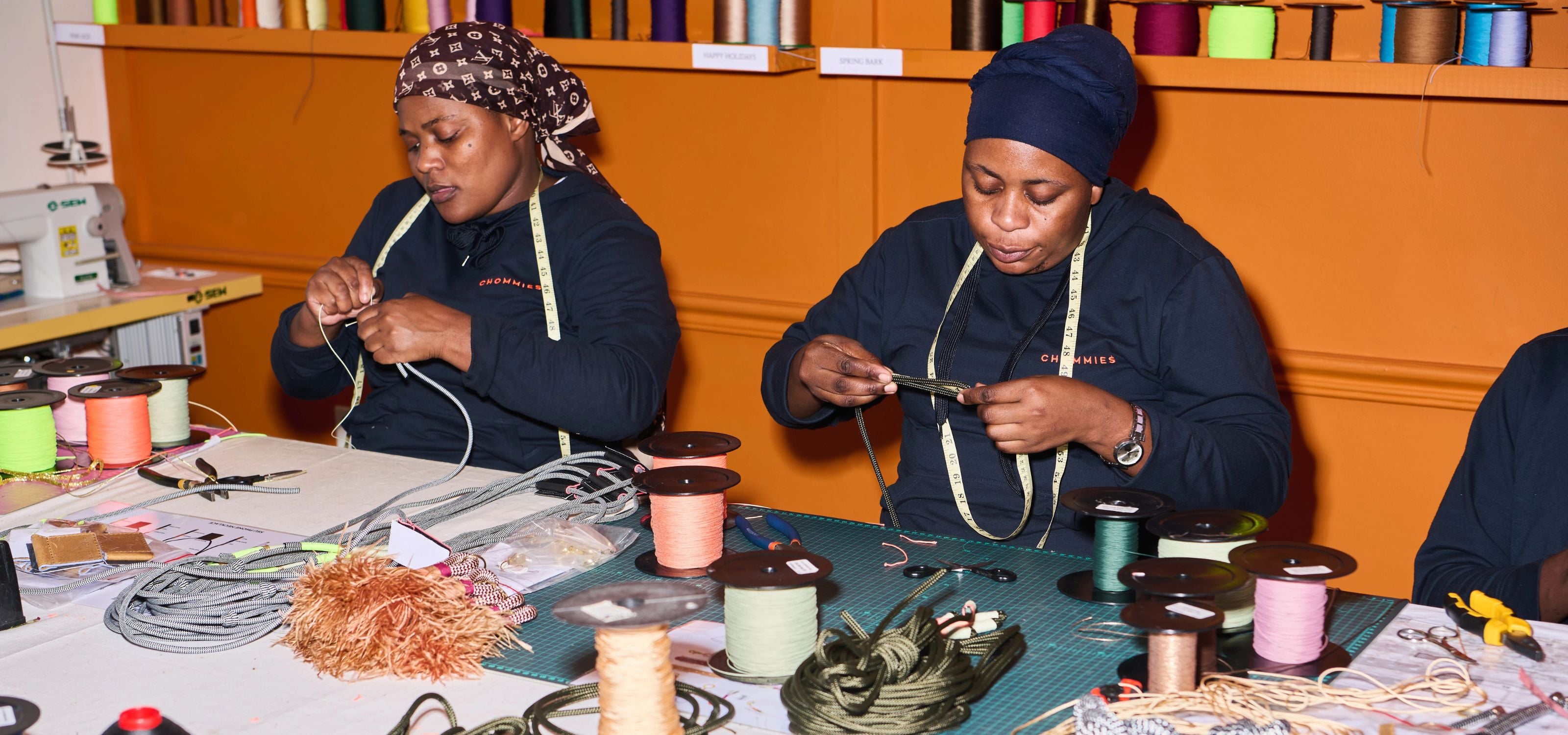 Two women working at a table with various materials and tools in a workshop setting.