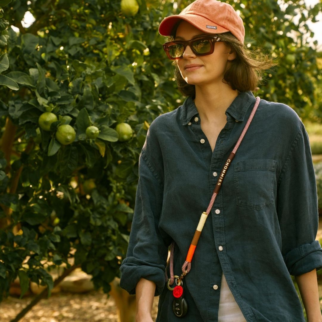 Woman in a green shirt and red cap standing in an orchard with green apples on trees wearing a high qua lanyard quality Chommies lanyard