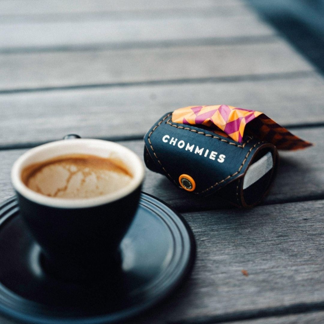 Cup of coffee on a saucer with a 'Chommies' Velcro poo bag product on a wooden surface