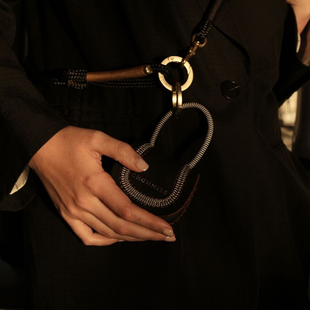 Hand holding a metallic keychain with a dark coat in the background
